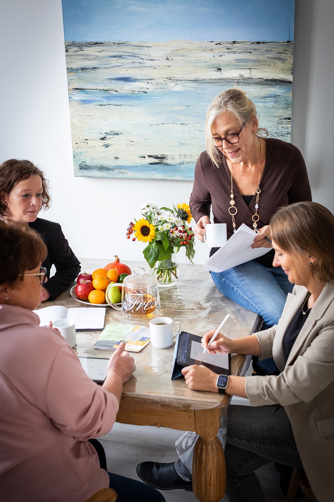 Ein Team des PKD Coesfeld bei einem harmonischen Hausbesuch, umgeben von Blumen und Früchten am Tisch.