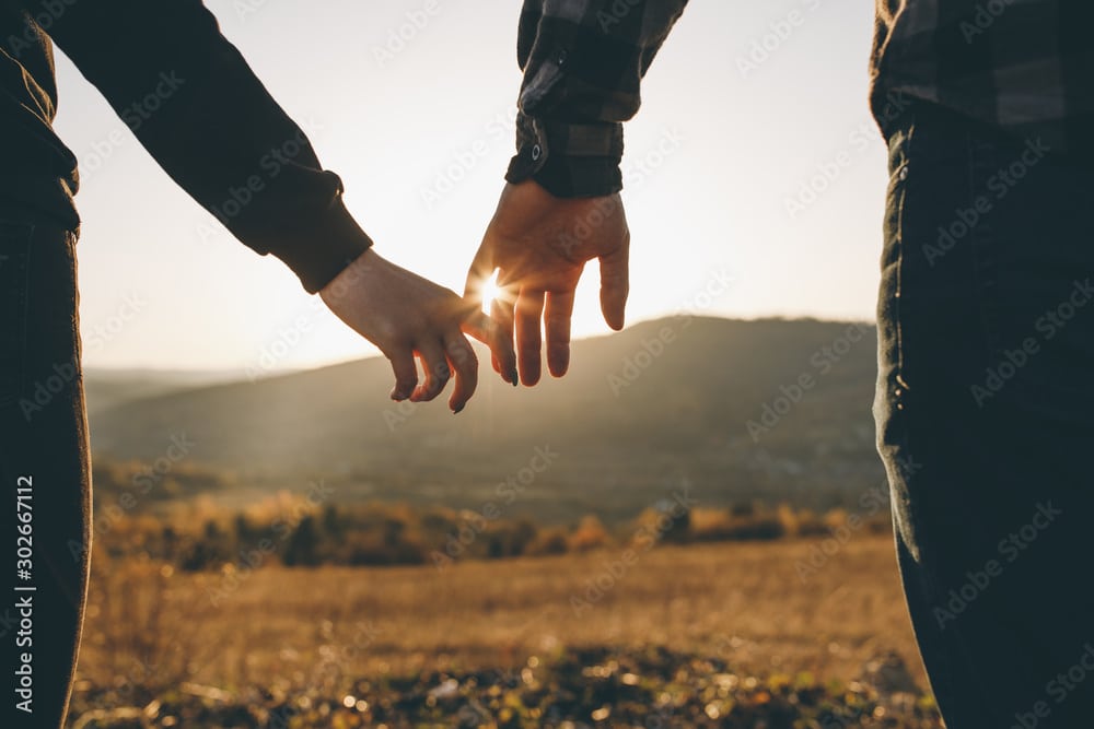 Zwei Menschen halten sich bei Sonnenuntergang die Hand, symbolisieren Unterstützung und Nähe in schwierigen Zeiten